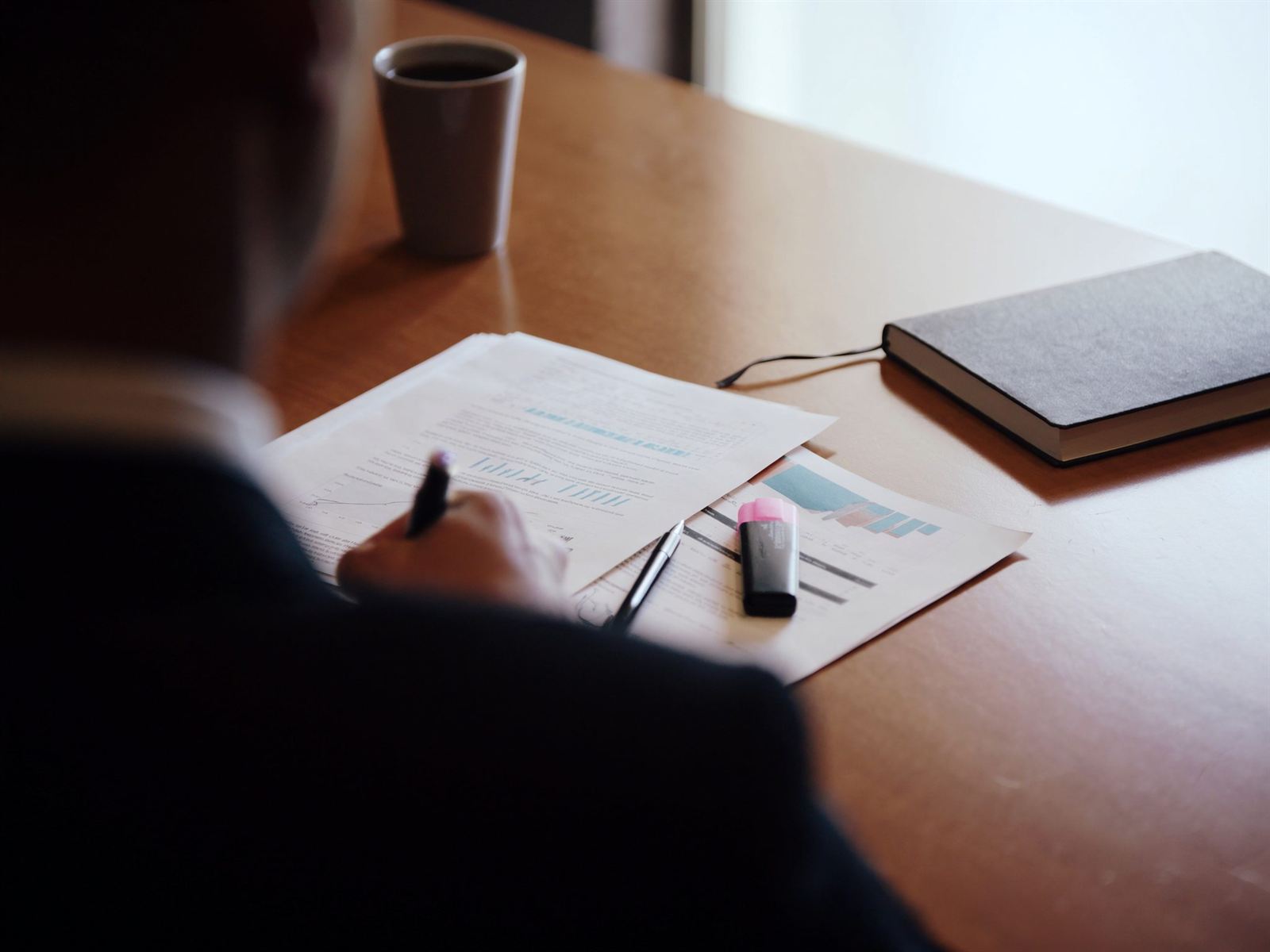 A professional marking up printed local market research with a pen beside a highlighter and a notebook